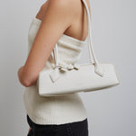 Person wearing a white sweater and holding a matching handbag against a plain background