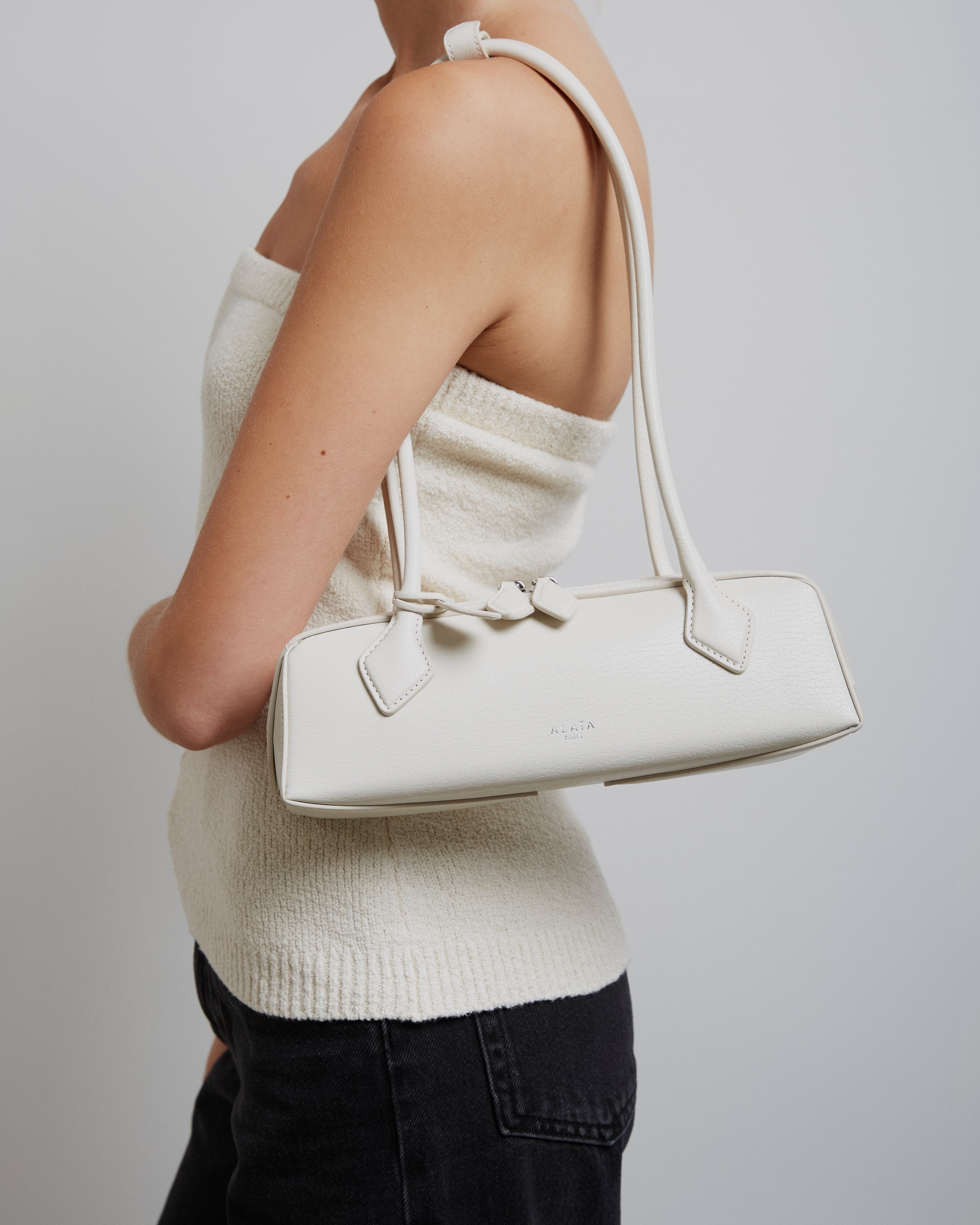 Person wearing a white sweater and holding a matching handbag against a plain background