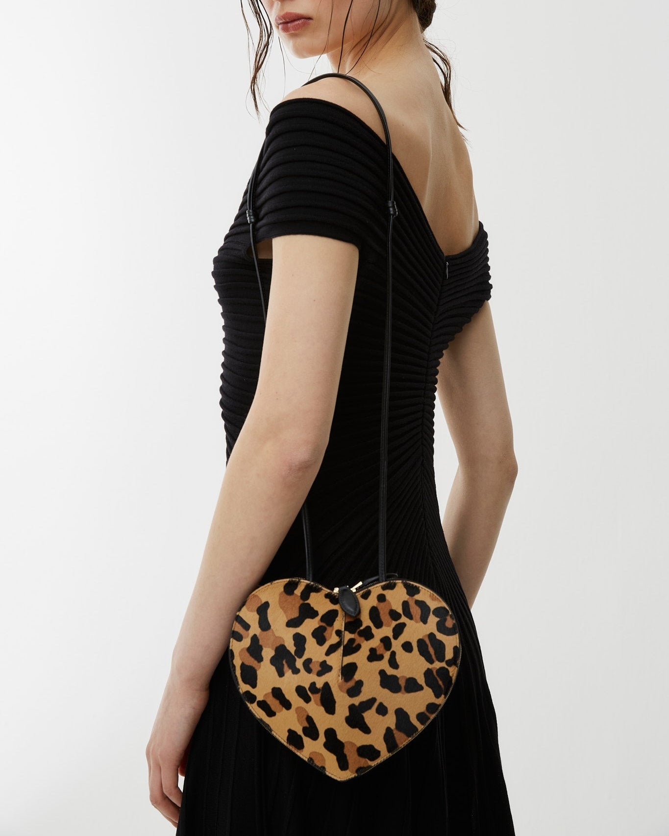 Woman holding a heart-shaped clutch with leopard print design on a white background