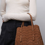 Person wearing a white sweater and holding a brown perforated handbag against a plain background