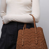 Person wearing a white sweater and holding a brown perforated handbag against a plain background