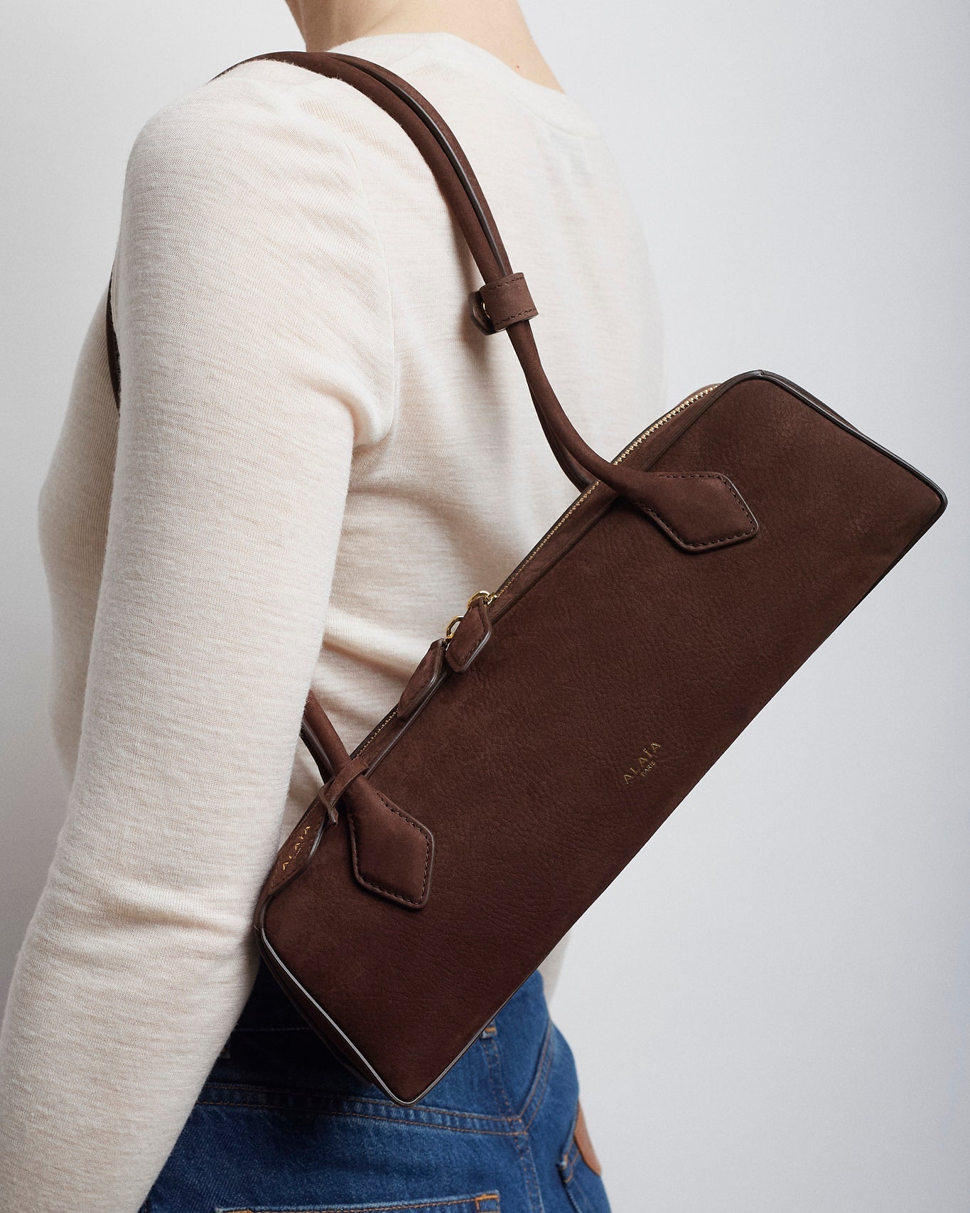 Person wearing a brown leather crossbody bag on a plain background