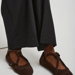 Brown ballet flats worn with black pants on a white background