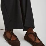 Brown ballet flats worn with black pants on a white background