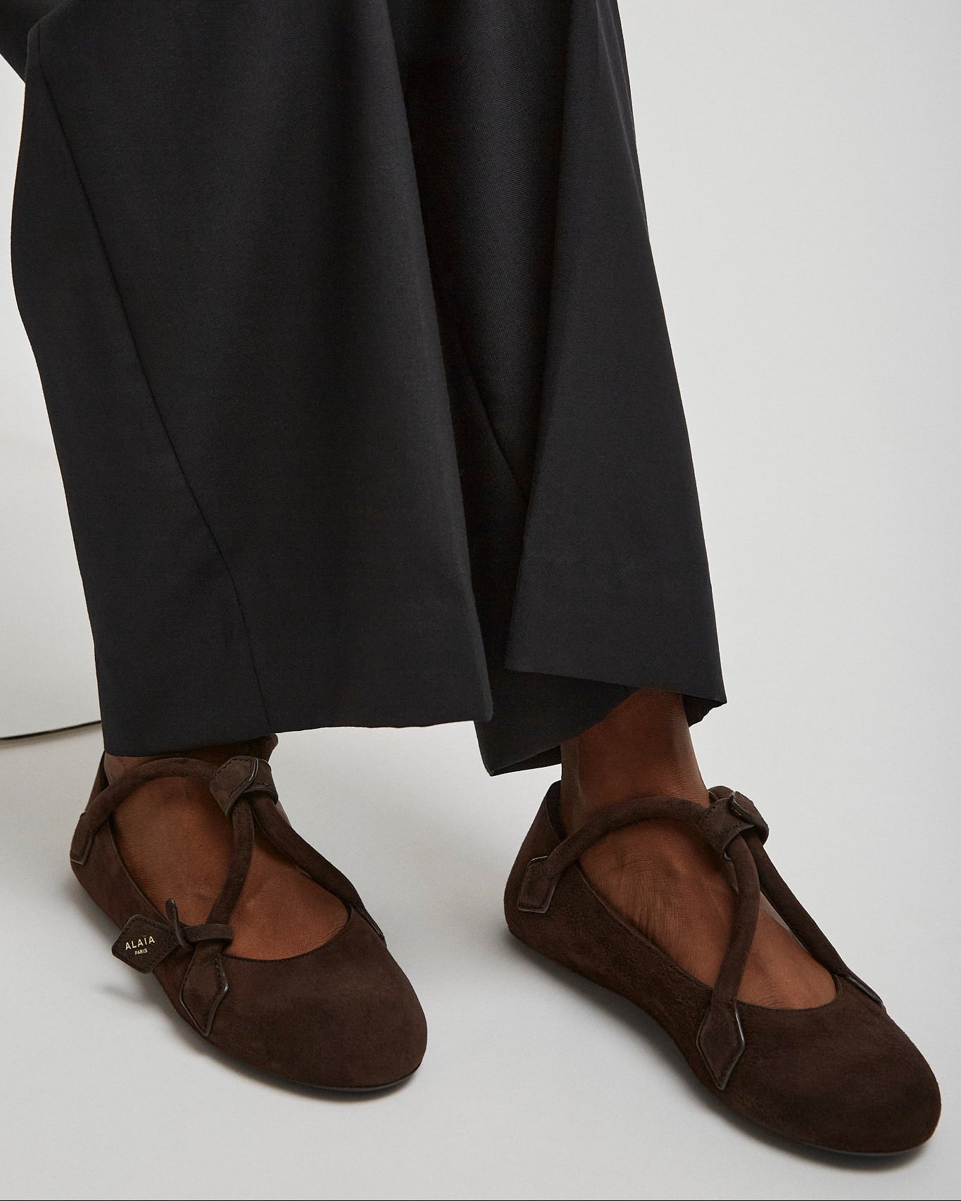 Brown ballet flats worn with black pants on a white background