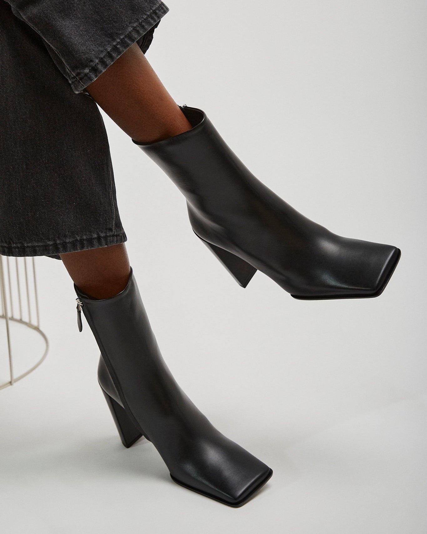 Black ankle boots worn with a black skirt on a light gray background