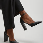 Black high-heeled shoes worn with black pants on a light gray background