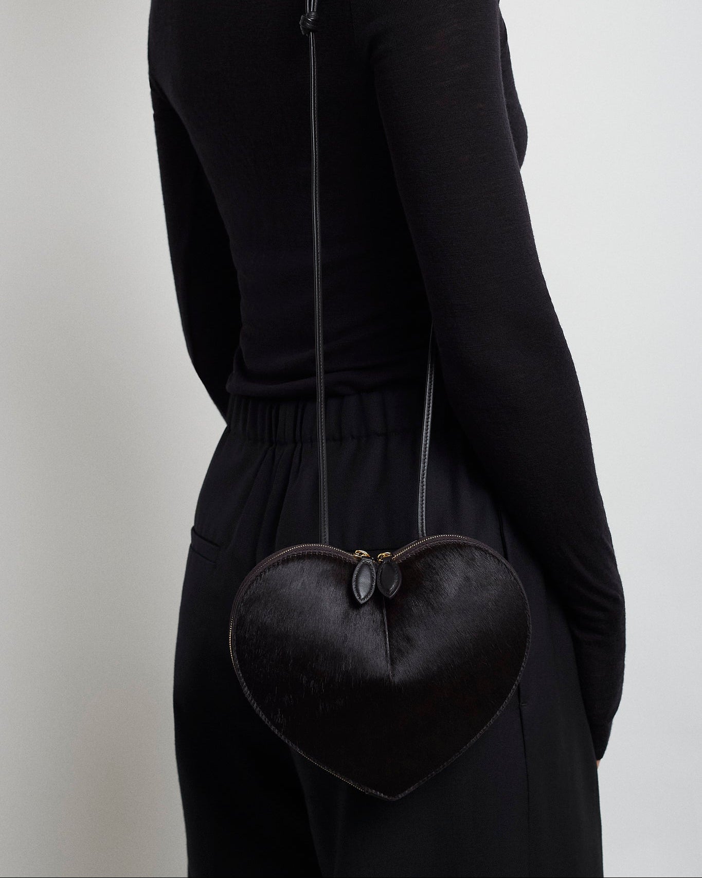 Person wearing a black heart-shaped bag on a plain background