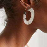 Silver hoop earring worn by a person with a neutral background