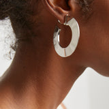 Silver hoop earring worn by a person with a neutral background