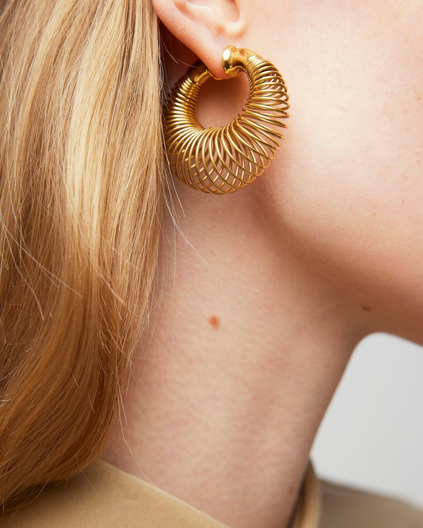 Gold hoop earring worn by a person with a neutral background