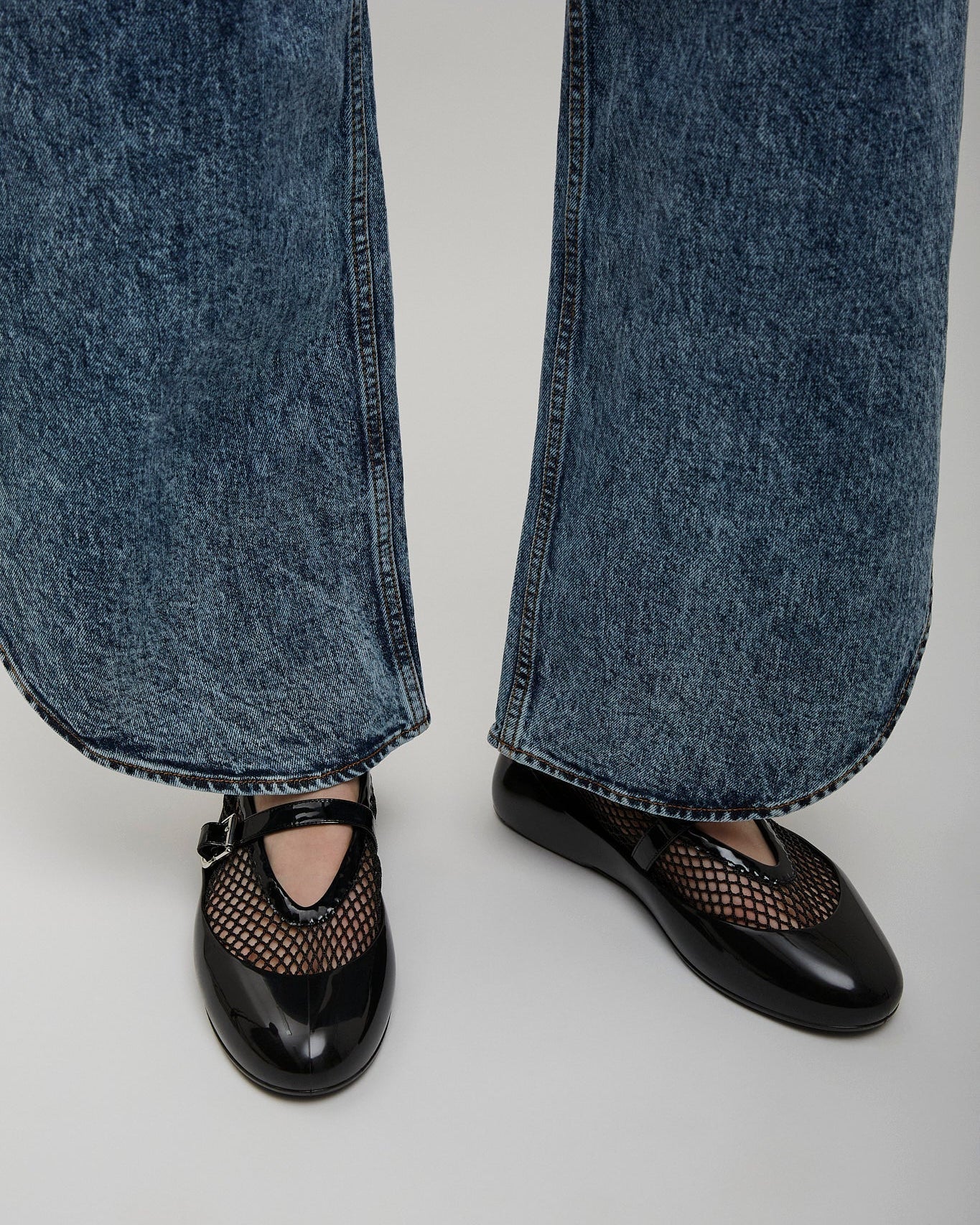 Black shoes with mesh design worn with blue jeans on a light gray background