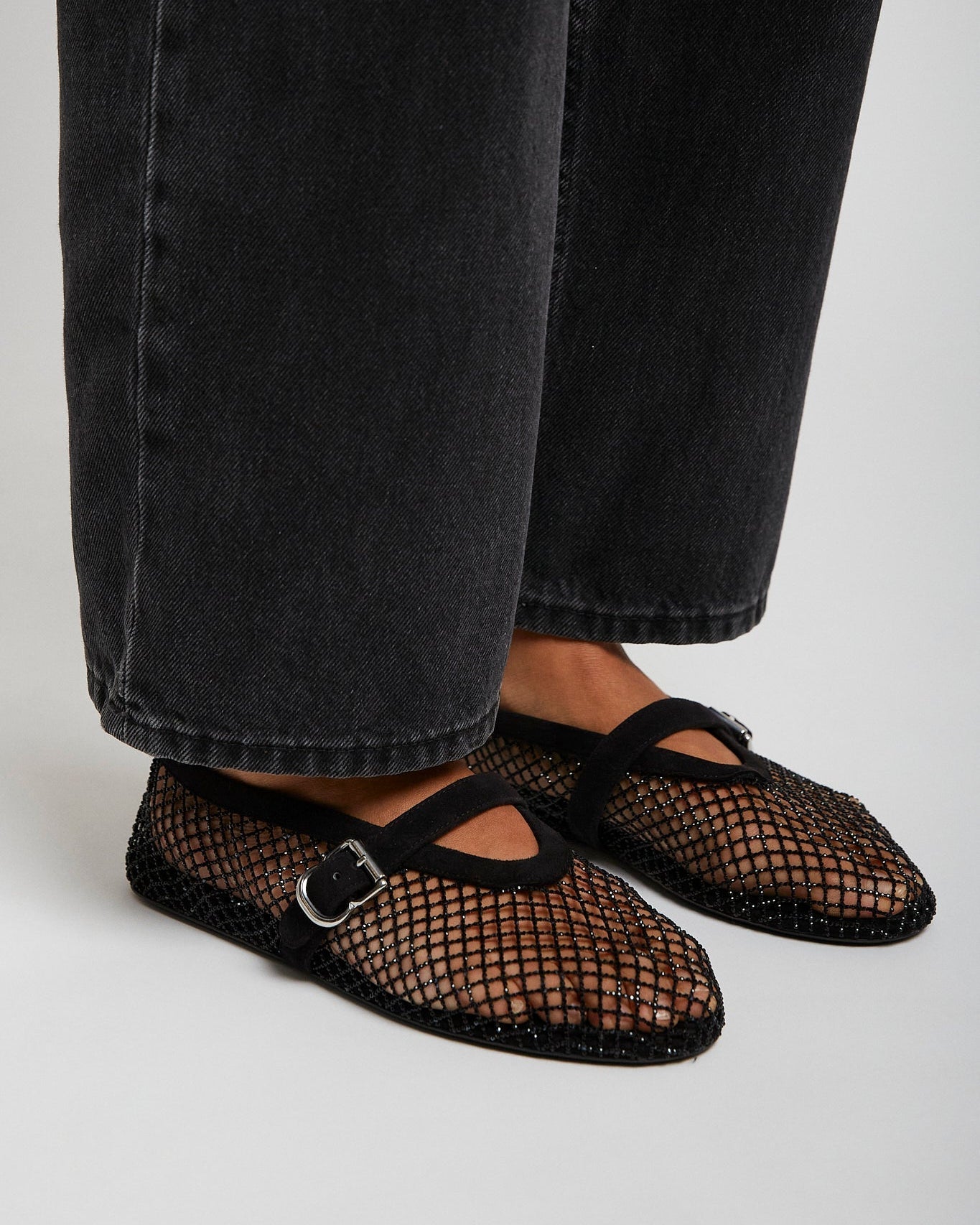 Black mesh shoes worn with black jeans on a light gray background