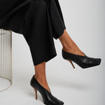 Person wearing black high-heeled shoes and black pants on a white background