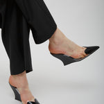 Black high-heeled shoes worn with black pants on a light gray background