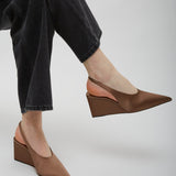 Brown wedge shoes worn with black jeans on a light gray background