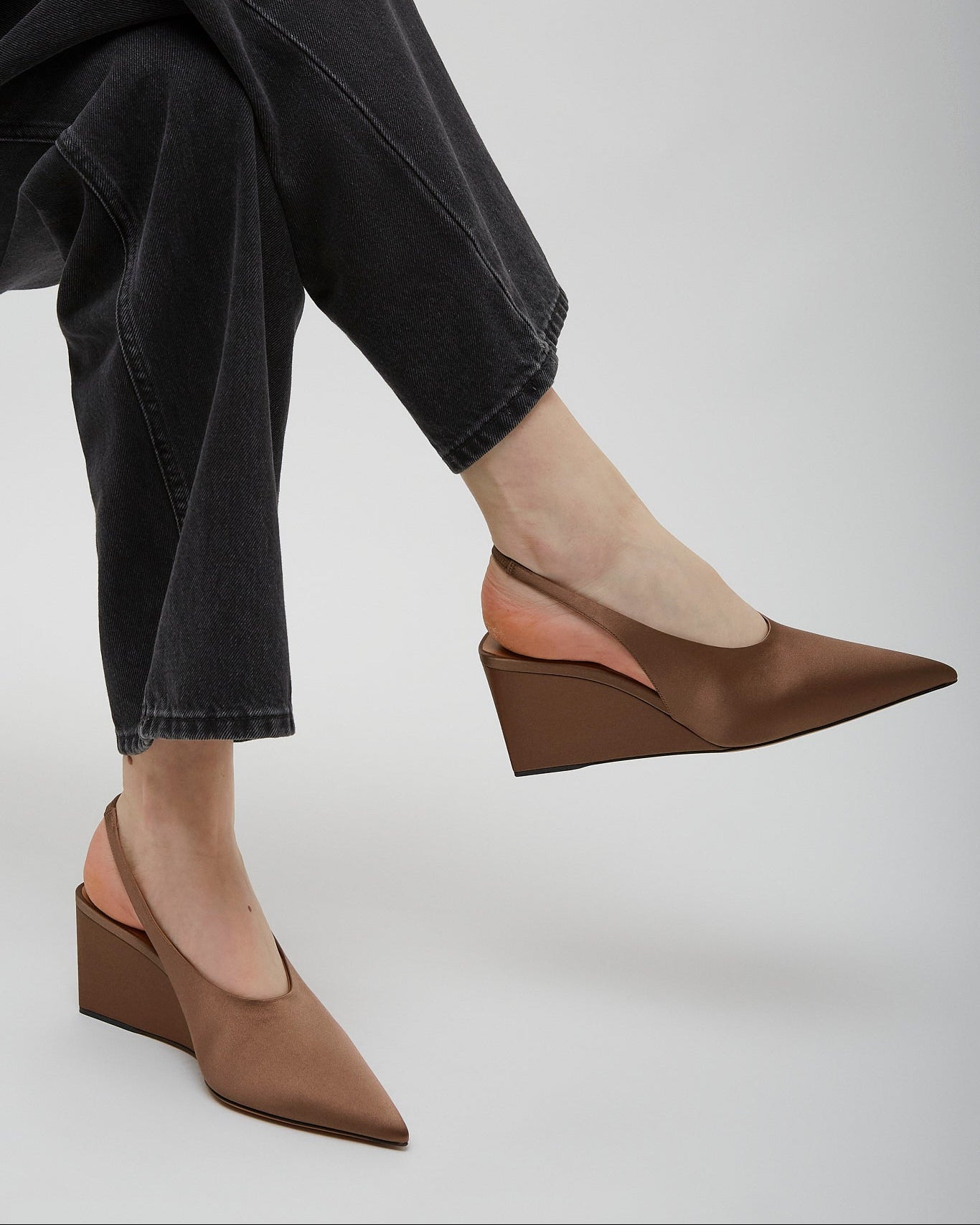 Brown wedge shoes worn with black jeans on a light gray background