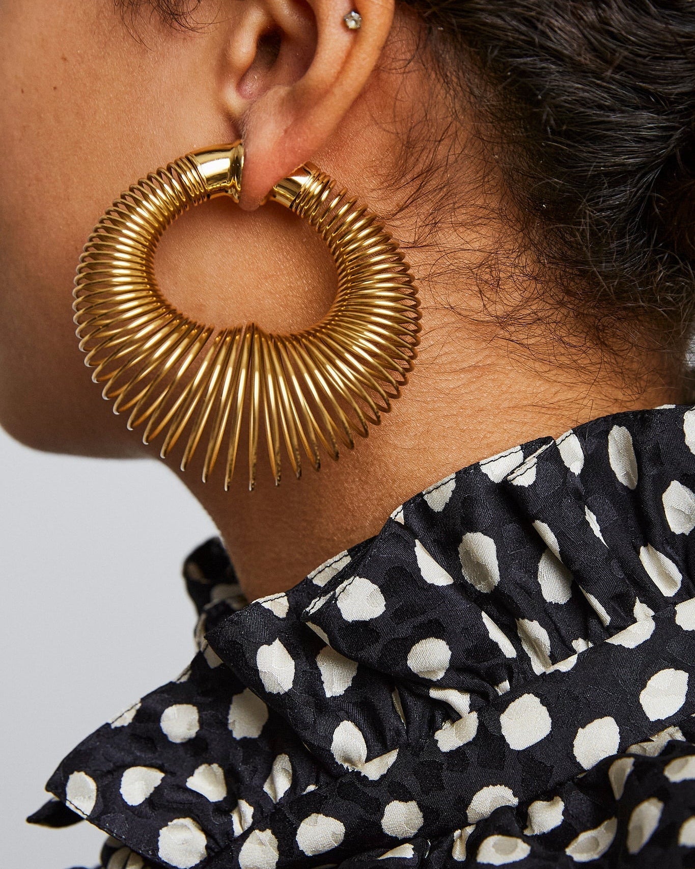 Close-up of a person wearing a gold hoop earring with a blurred background