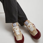 Beige and burgundy sneakers worn with black jeans on a white background