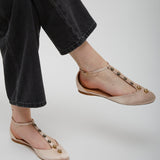 Beige flat shoes with embellishments worn with black pants on a light gray background