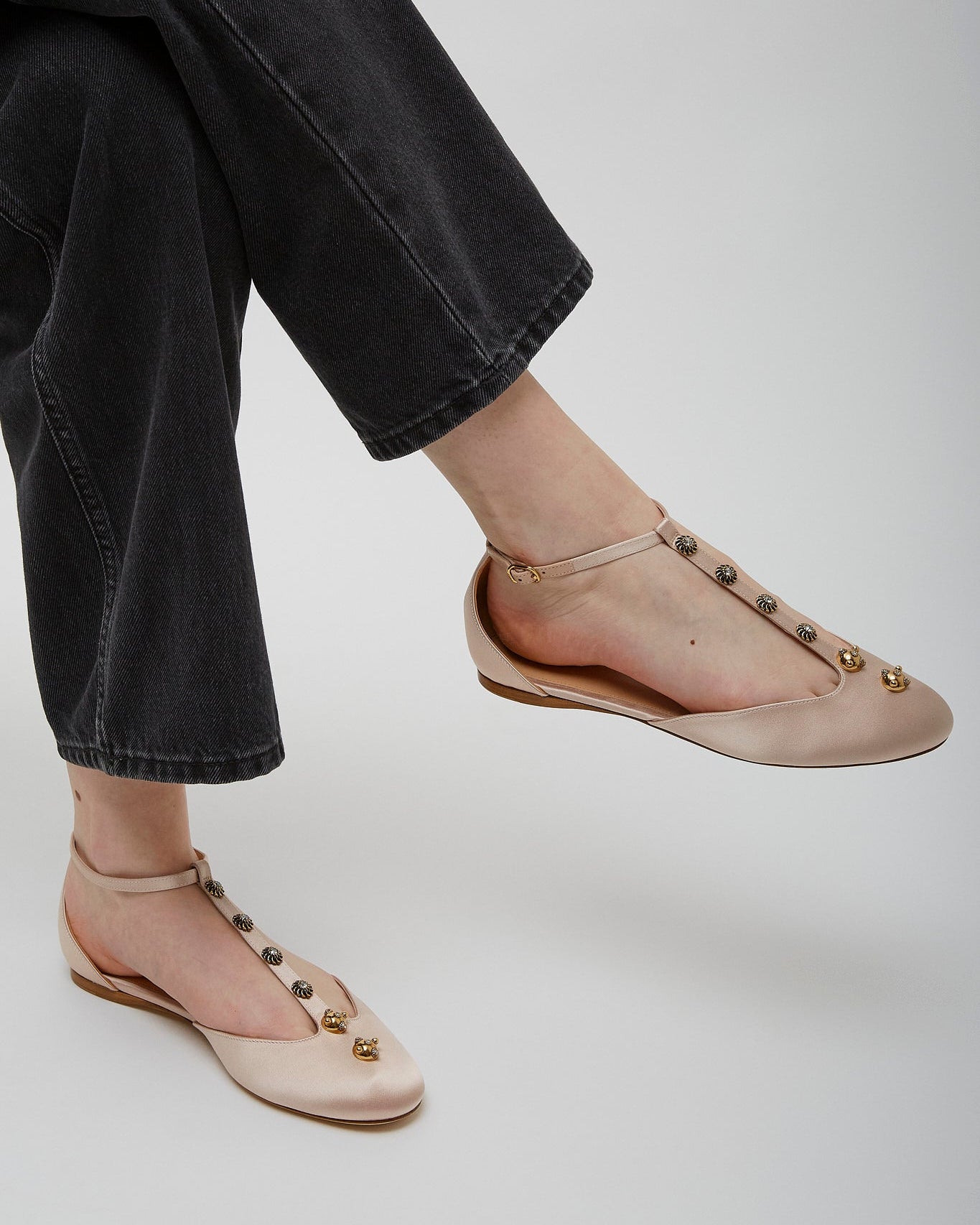 Beige flat shoes with embellishments worn with black pants on a light gray background