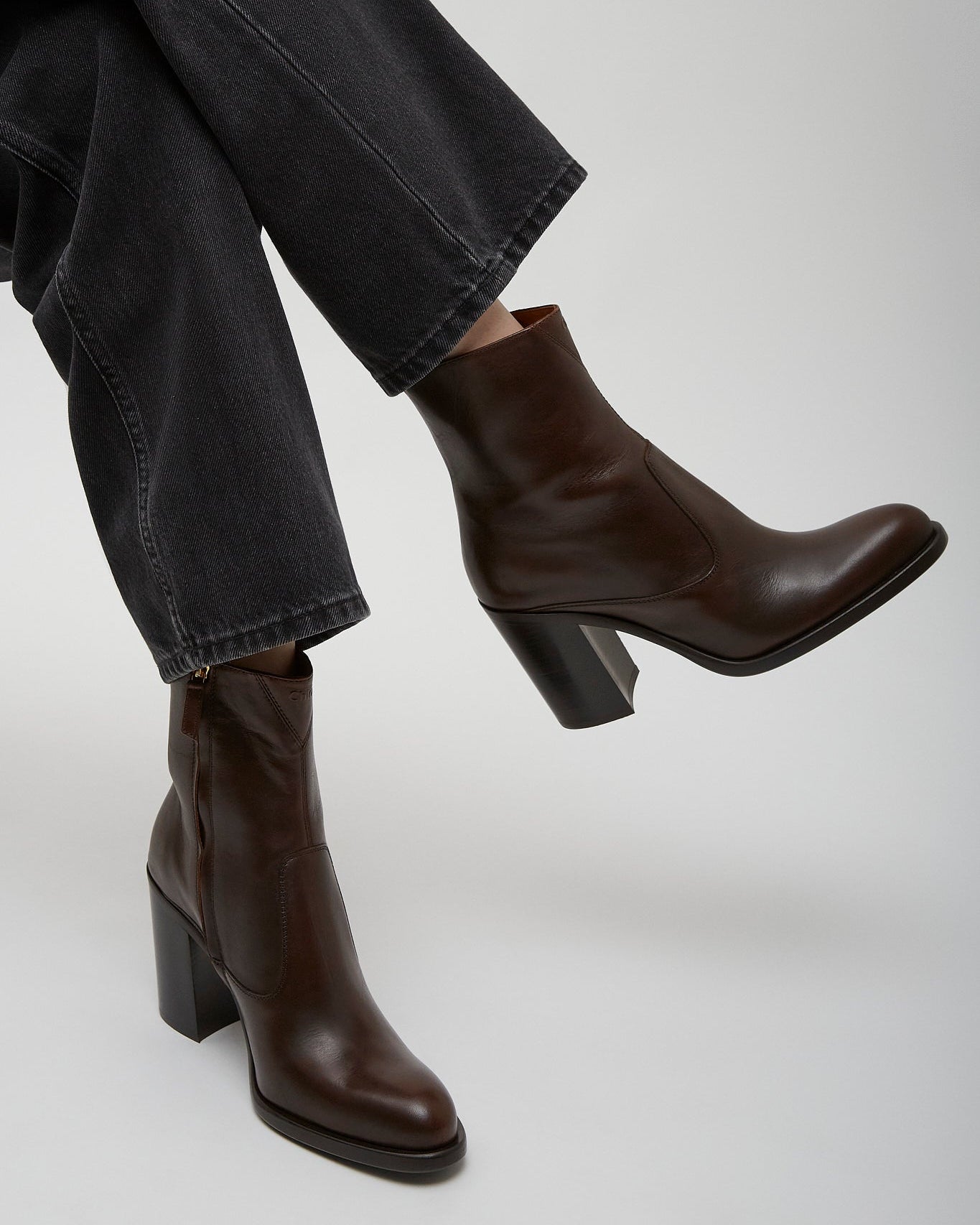 Brown leather ankle boots worn with dark jeans on a light gray background