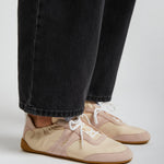Beige sneakers worn with black jeans on a light gray background