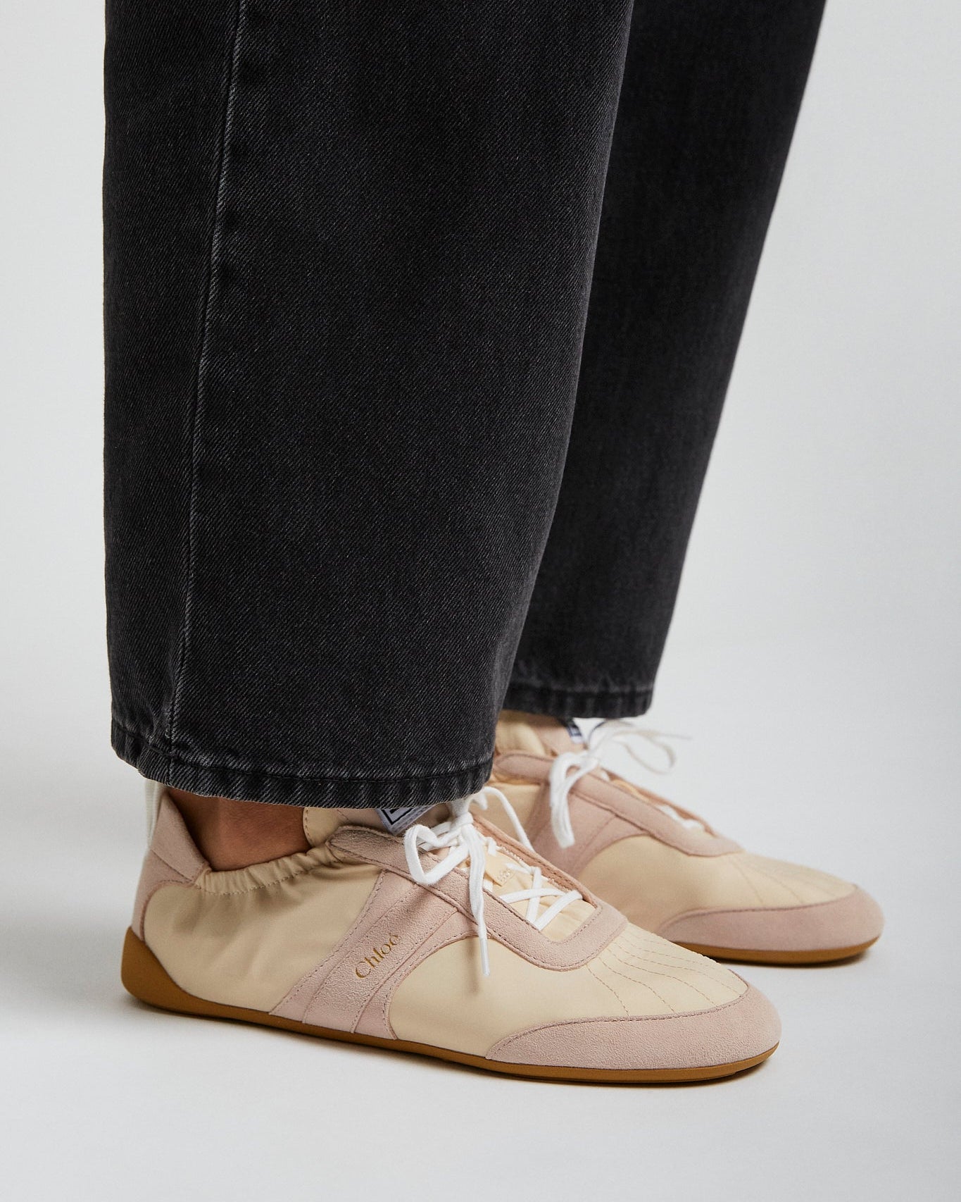 Beige sneakers worn with black jeans on a light gray background