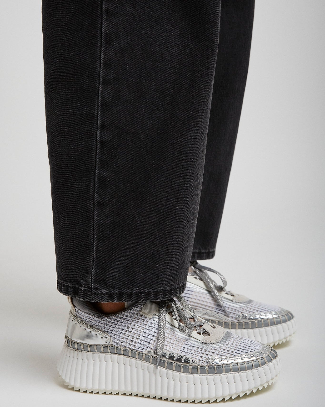 Silver high-top sneakers worn with black jeans on a light gray background
