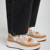 Person wearing black jeans and white sneakers with brown soles on a light gray background