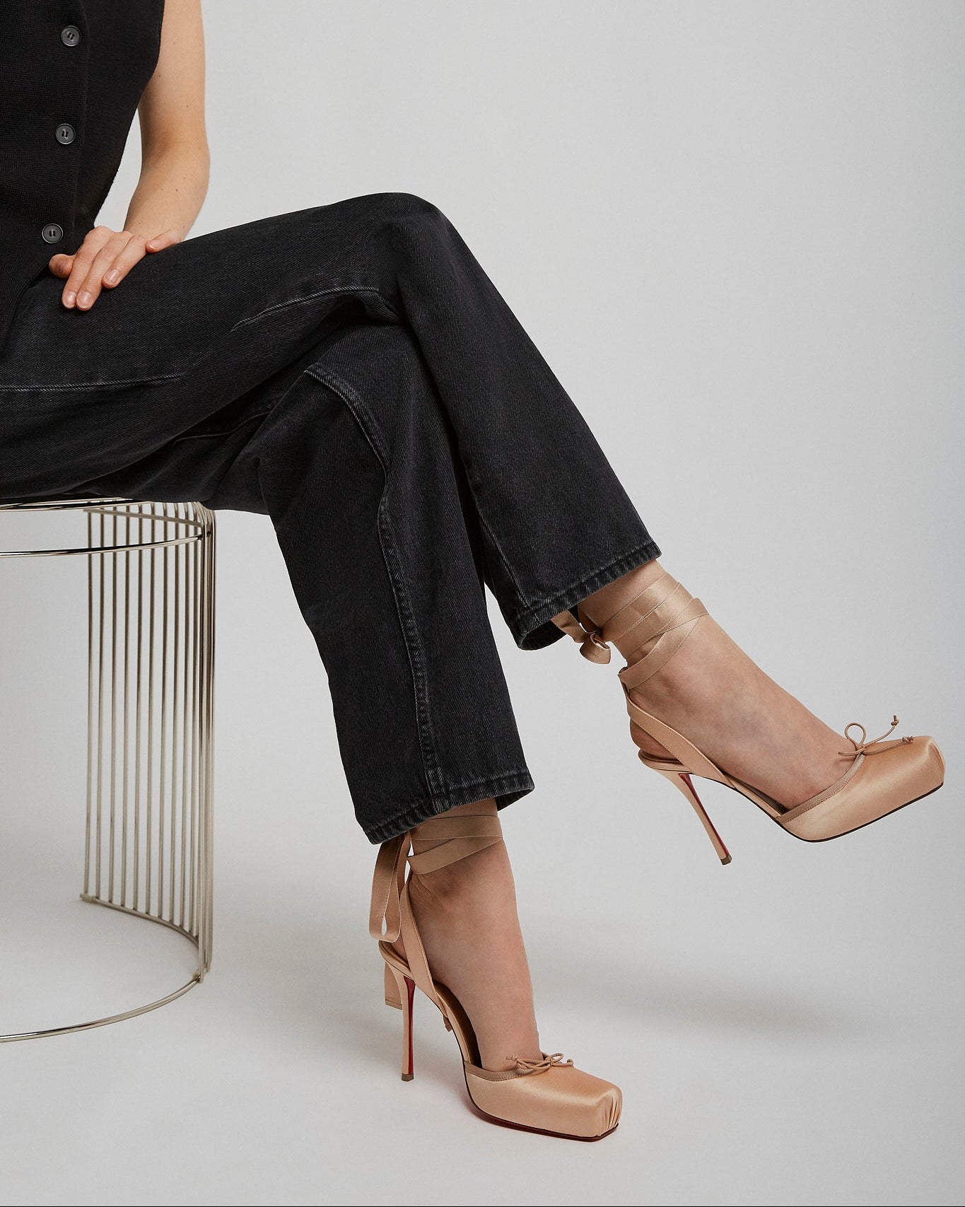 Person wearing black sleeveless top and jeans with beige high-heeled shoes on a white background