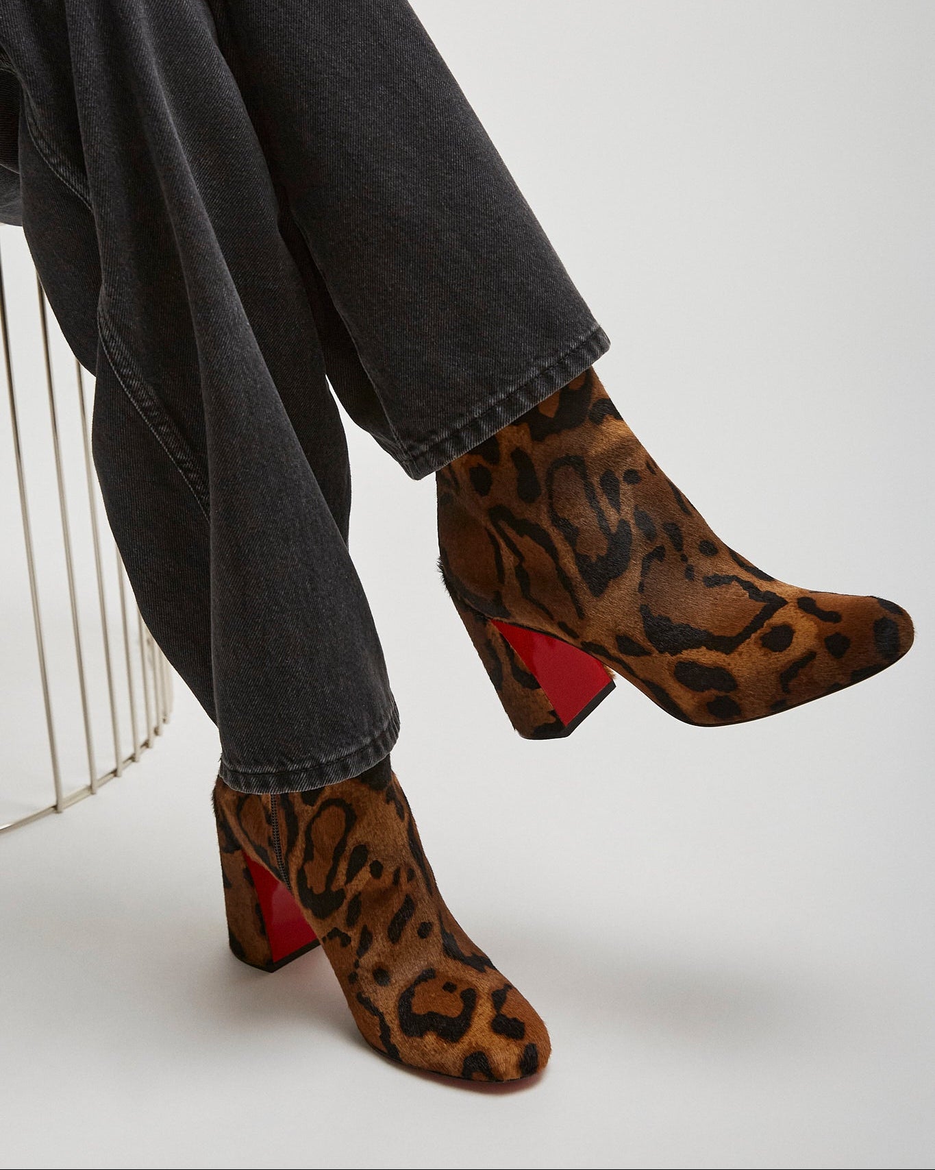 Leopard print boots with red soles worn by a person sitting on a white surface.
