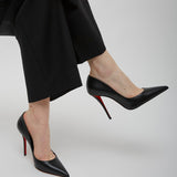 Person wearing black high-heeled shoes with red soles and black pants on a light gray background