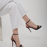 Black high-heeled sandals with red soles worn with white pants on a light gray background