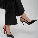 Black high-heeled shoes with red soles worn by a person in black pants on a light gray background