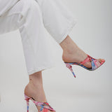 Multicolored high-heeled sandals worn with white pants on a light gray background