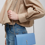Person wearing a beige jacket and blue jeans with a blue handbag on a plain background