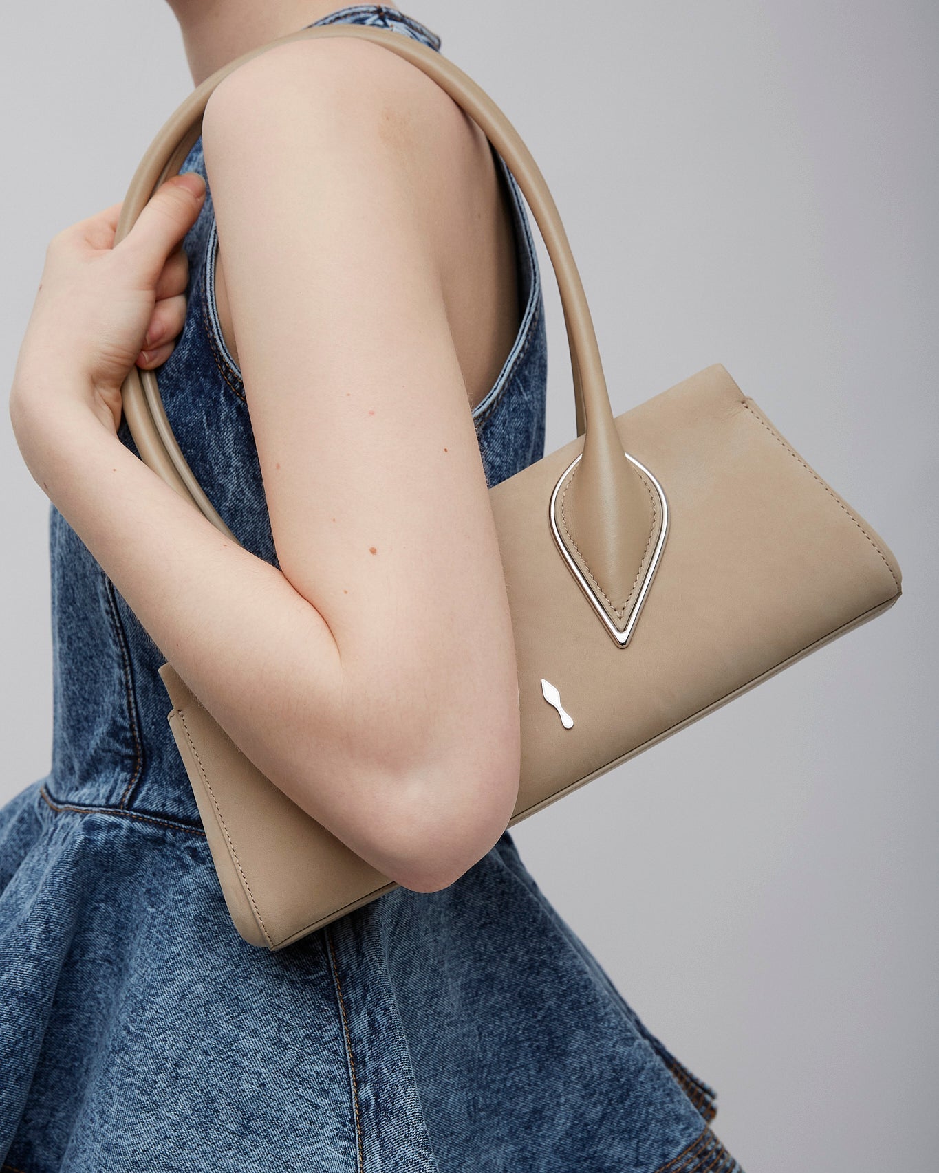Person holding a beige handbag with a gray background