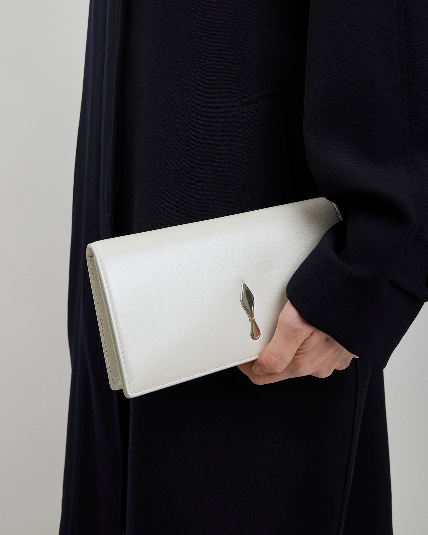 Person holding a white clutch with a subtle design against a neutral background