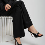 Person wearing a black outfit with high-heeled shoes sitting on a white stool against a light gray background