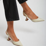 White high-heeled shoes worn with black jeans on a light gray background