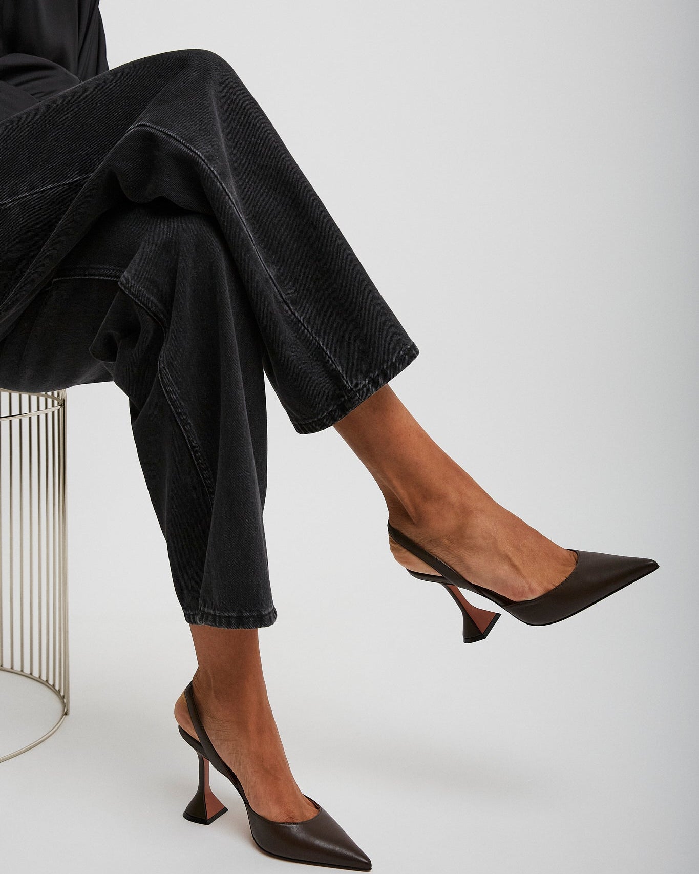 Person wearing black high-heeled shoes and dark pants sitting on a white background