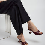 Person wearing black pants and brown high-heeled shoes sitting on a metal stool.