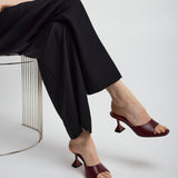 Person wearing black pants and brown high-heeled shoes sitting on a metal stool.