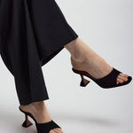 Person wearing black high-heeled shoes and black pants on a white background