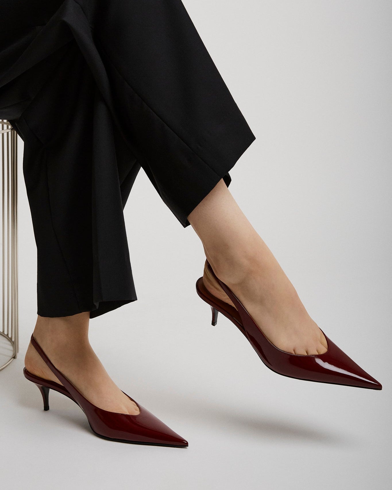 Person wearing black pants and red high heels on a light gray background