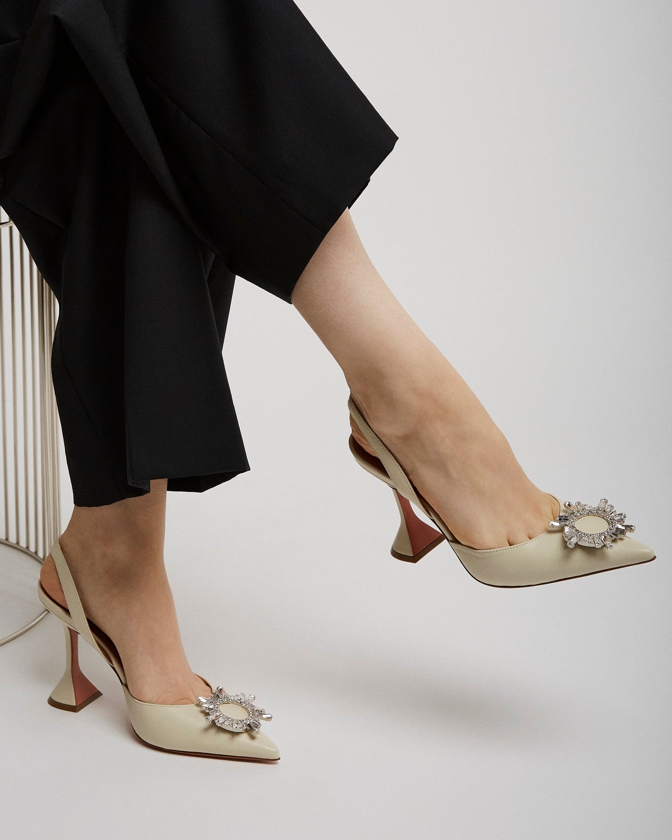 Person wearing black pants and beige high-heeled shoes with decorative elements on a white background