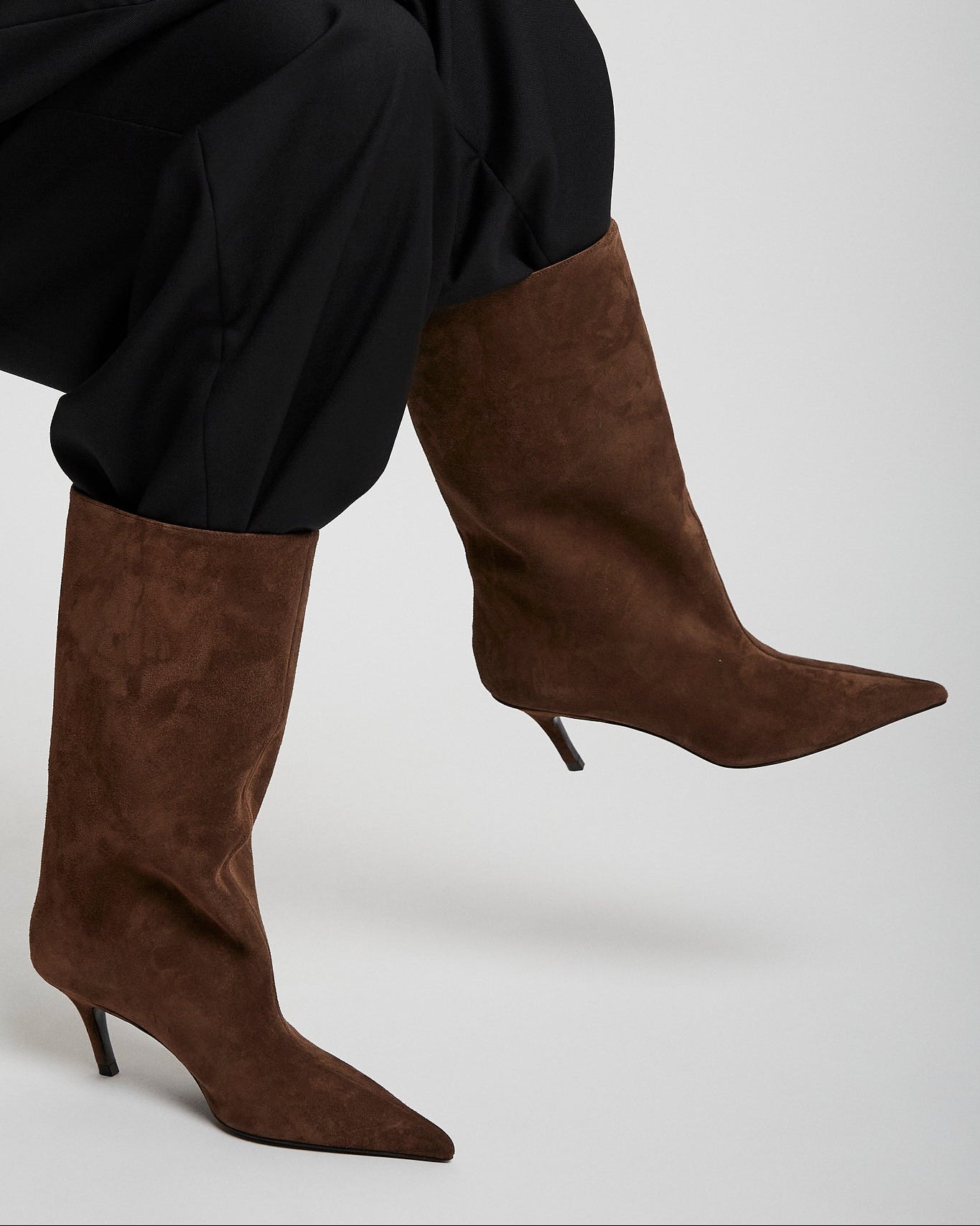 Brown knee-high boots worn with black pants on a light gray background