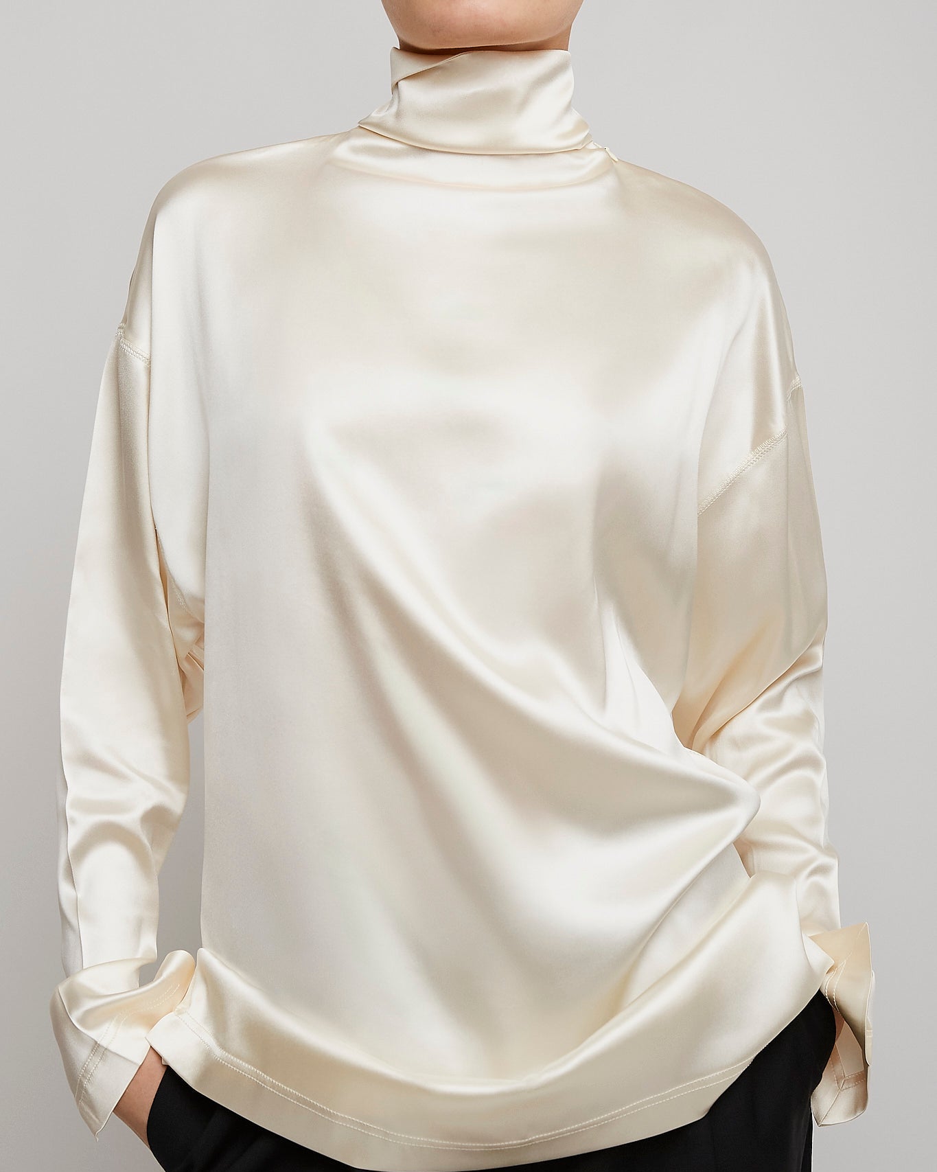 Person wearing a cream-colored long-sleeve top against a gray background