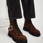 Brown suede boots with black soles worn with dark jeans on a white background